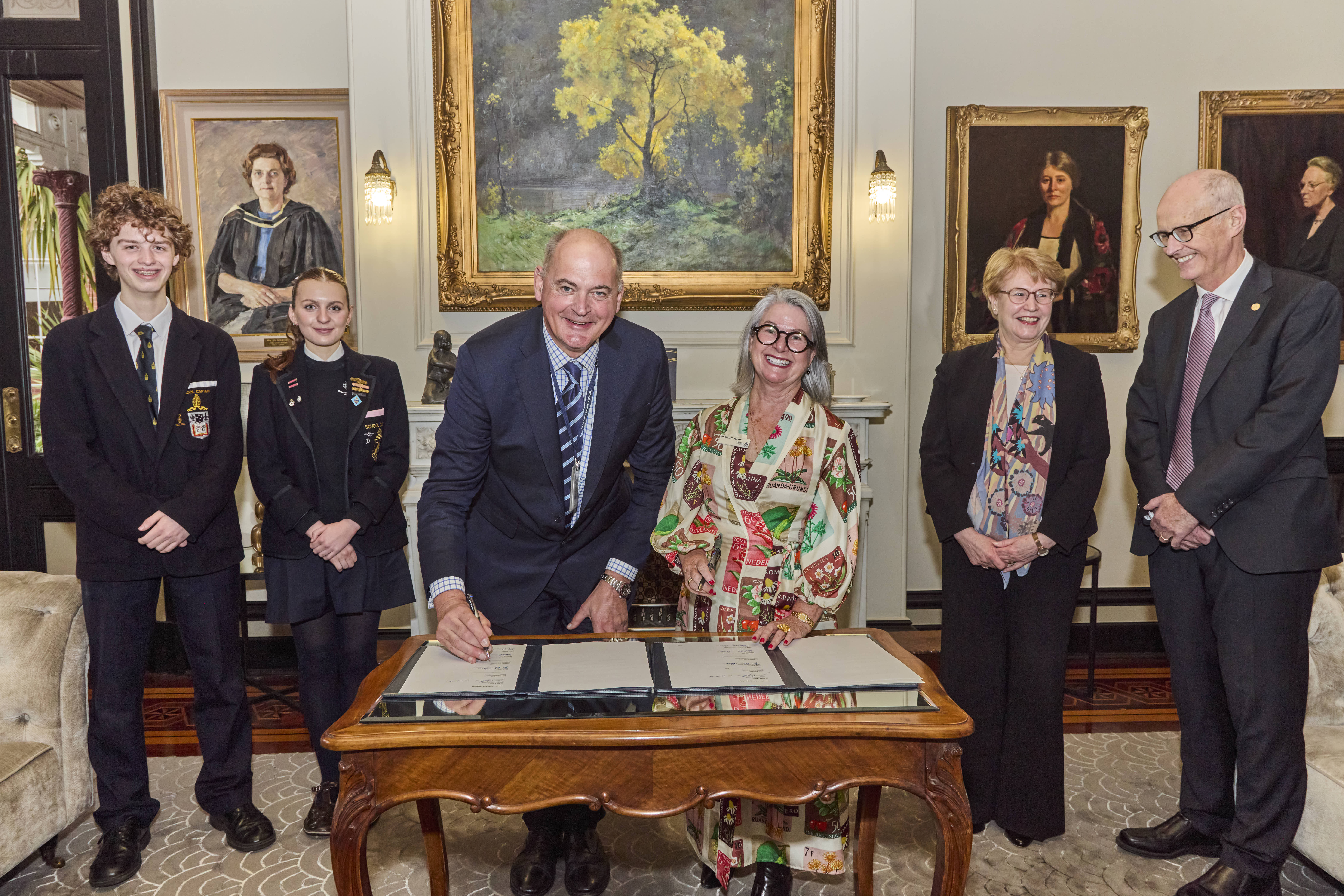 Edgar (Captain, Melbourne Grammar School), Xanthe (Captain, Melbourne Girls Grammar), Philip Grutzner (Headmaster, Melbourne Grammar School), Dr Toni E Meath (Principal, Melbourne Girls Grammar), Diana Nicholson (Chair of School Council, Melbourne Girls Grammar), Professor Julian Smith (Chair of School Council, Melbourne Grammar School) sign the Memorandum of Understanding.